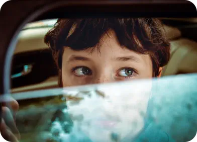 A young boy looks worriedly out of a car window