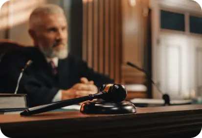 A judge in a black robe sits in court holding a gavel
