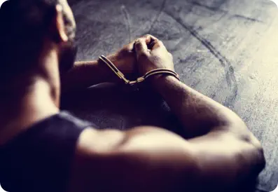 The shoulder, arms and hands of a man sitting at a table with handcuffs on